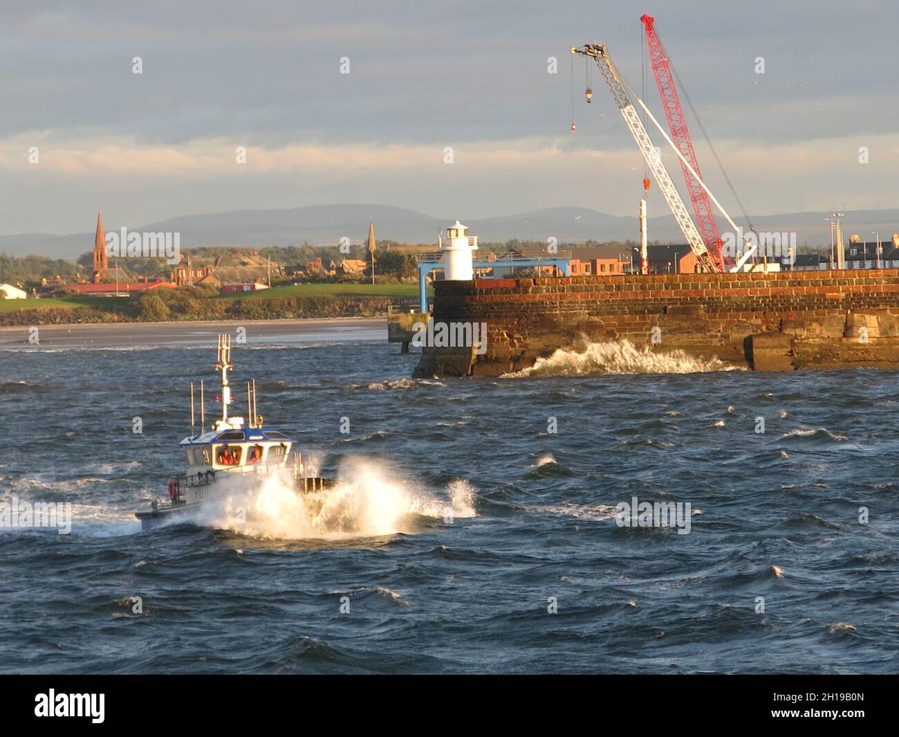 Spruzzi bianchi di fronte alla barca pilota su acque irregolari che escono dal porto di Troon presso il faro Foto Stock