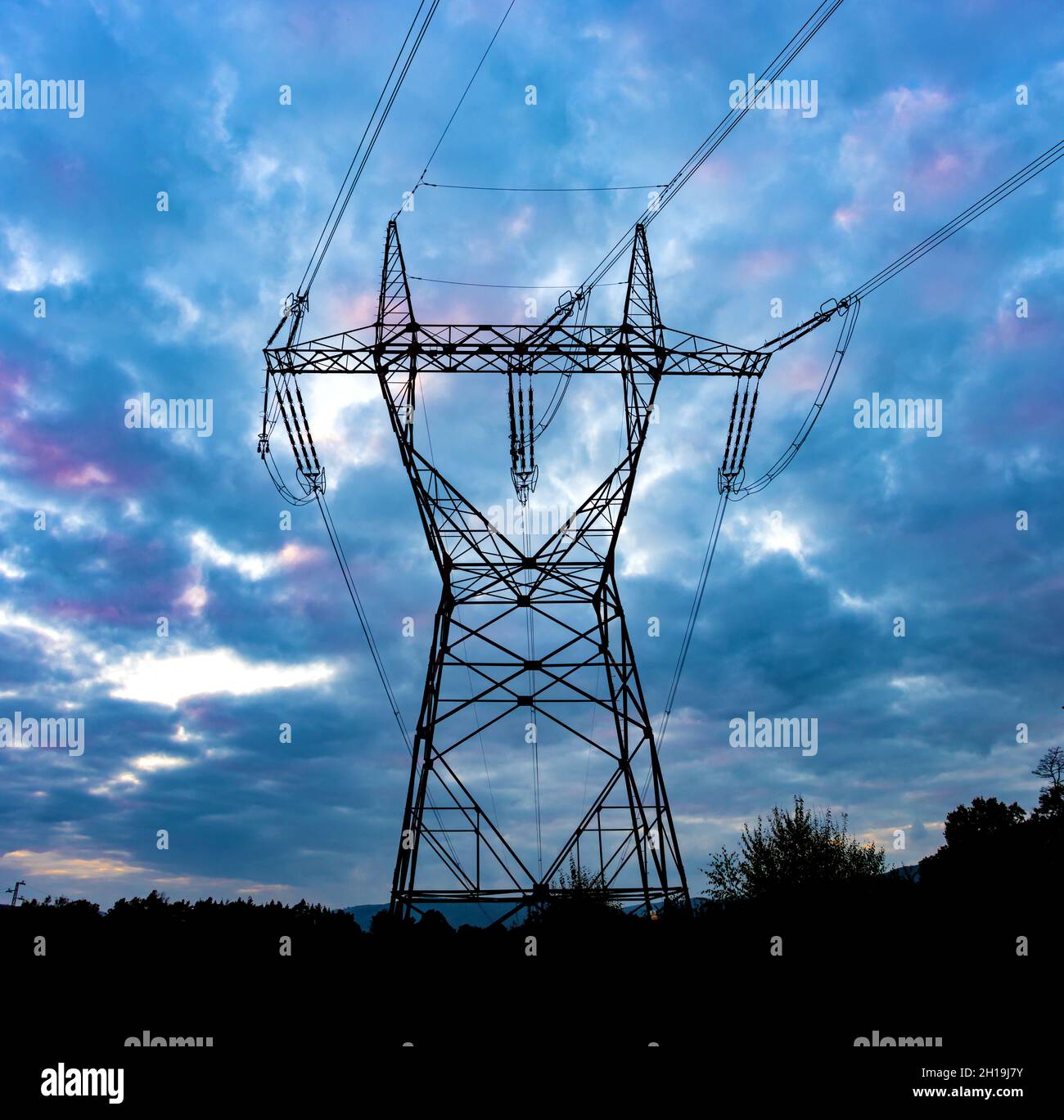 Silhouette di una torre ad alta tensione con le nuvole al tramonto sullo sfondo Foto Stock