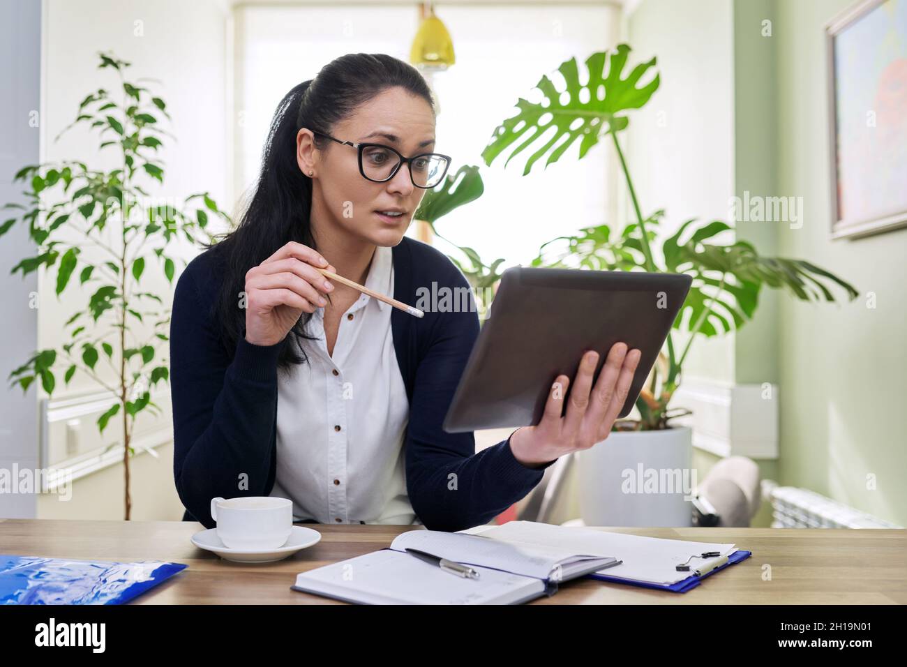 Donna di mezza età che lavora a casa utilizzando un tablet digitale per videochiamate e conferenze Foto Stock