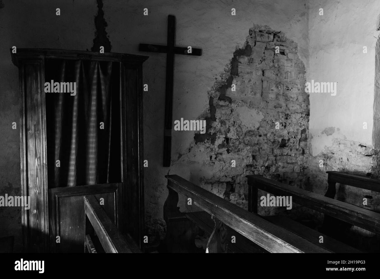 Un primo colpo di un vecchio muro danneggiato di una chiesa con panchine di legno e una croce accanto ad essa Foto Stock