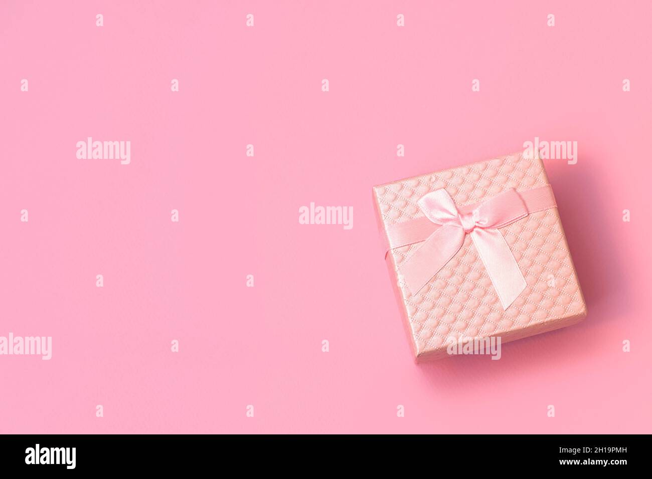 Vista dall'alto della confezione regalo rosa con arco in raso su sfondo rosa pastello con spazio per la copia. Composizione piatta per matrimonio, compleanno, Felice giorno della donna, giorno delle madri, San Valentino. Foto Stock