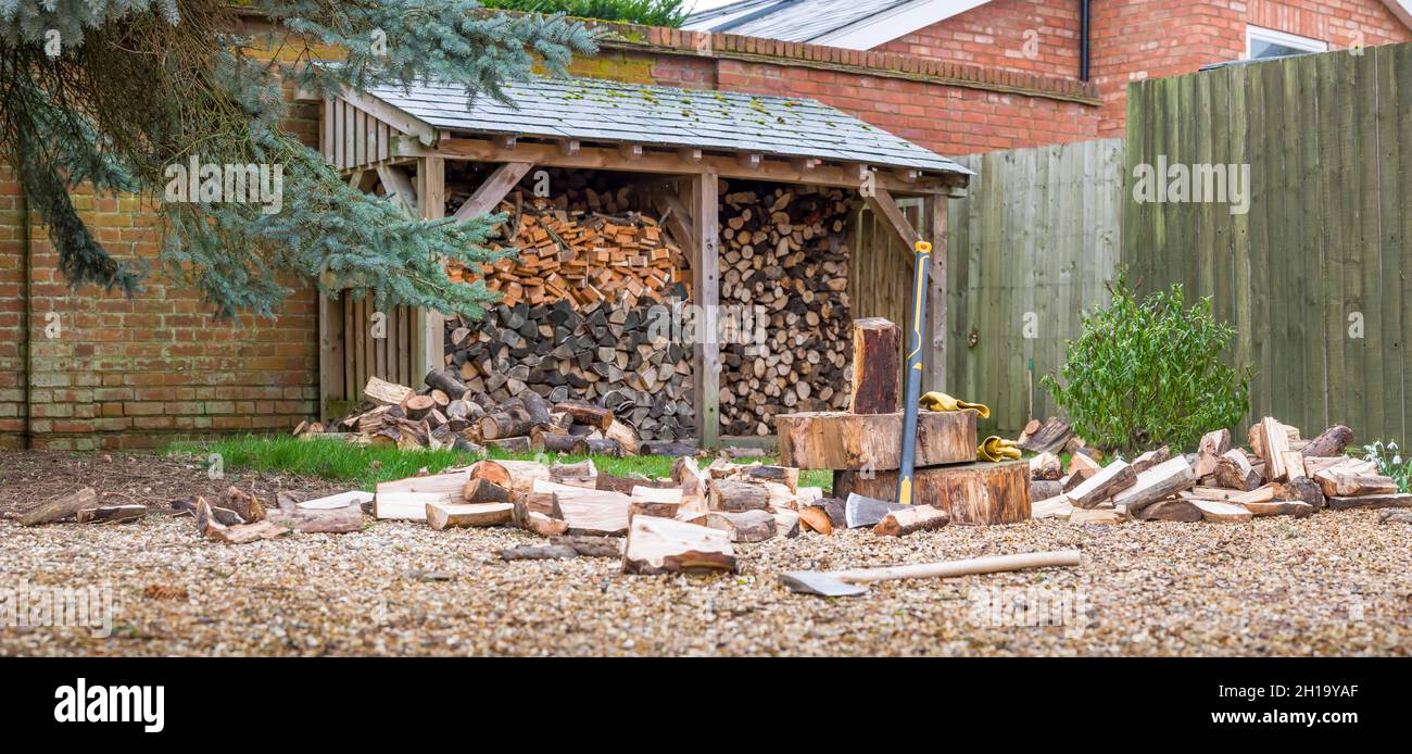 Legna da ardere pali di tronchi con ascia e maul spaccato. Panorama giardino inglese raffigurante l'energia rinnovabile, concetto di biocarburante Foto Stock