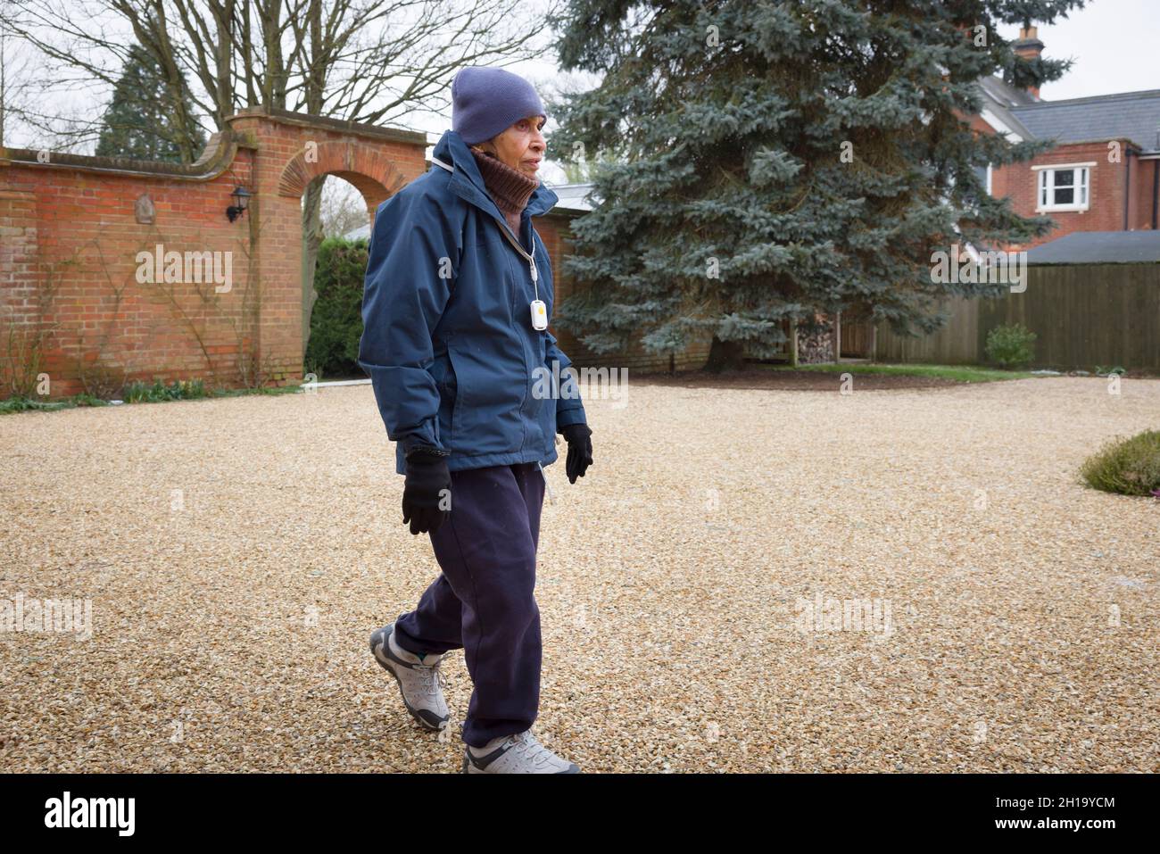 Donna asiatica britannica anziana che cammina all'aperto in inverno. Può rappresentare l'attività fisica o la vita di un anziano in una casa di cura o in una casa di cura del Regno Unito. Foto Stock