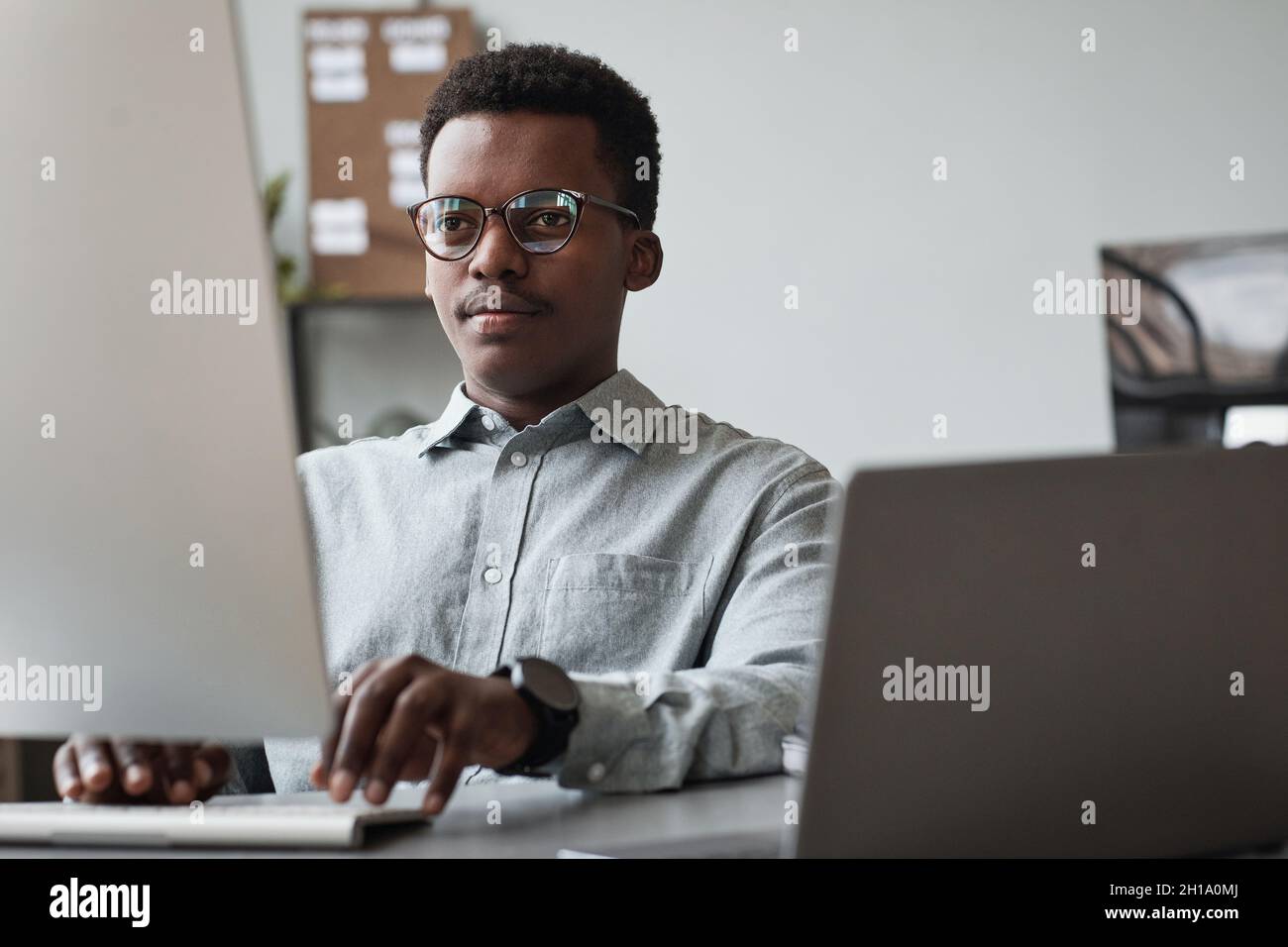 Vista frontale ritratto di giovane uomo afroamericano usando il computer e scrivere codice in ufficio di sviluppo software, spazio di copia Foto Stock