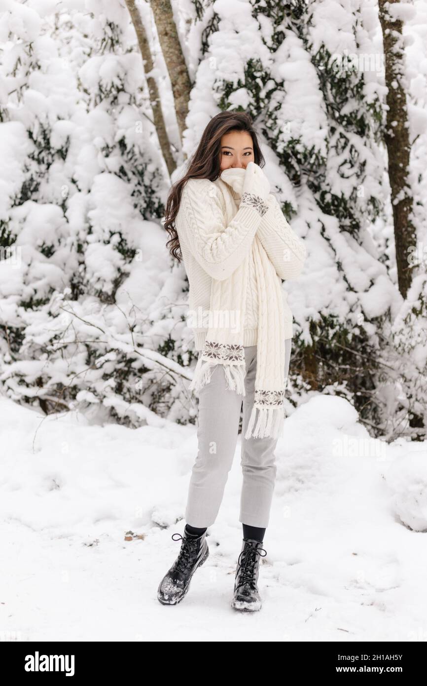 Cute Asian Girl in piedi sorridente nella foresta invernale. Inverno nevoso giorno. Bella ragazza Foto Stock