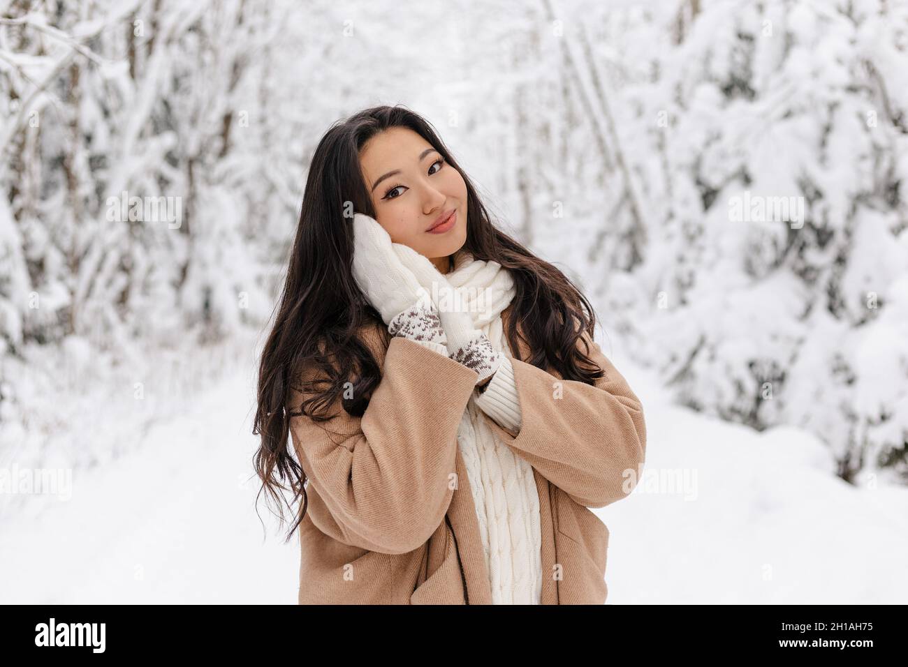 Cute Asian Girl in piedi sorridente nella foresta invernale. Inverno nevoso giorno. Bella ragazza Foto Stock