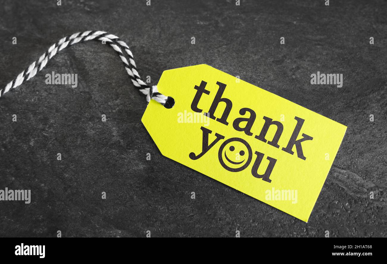 Grazie segno di ringraziamento e messaggio di testo su un'etichetta di prezzo di carta gialla su sfondo grigio scuro. Foto Stock