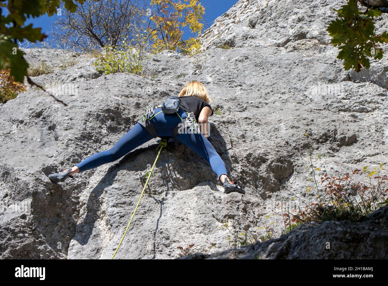 Giovane donna che arrampica parete rocciosa naturale alta Foto Stock