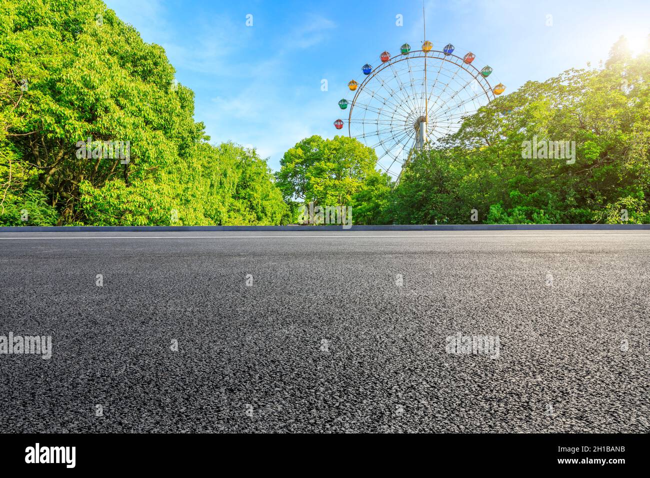 Strada asfaltata vuota e ruota di ferro con foresta verde sotto il cielo blu. Foto Stock