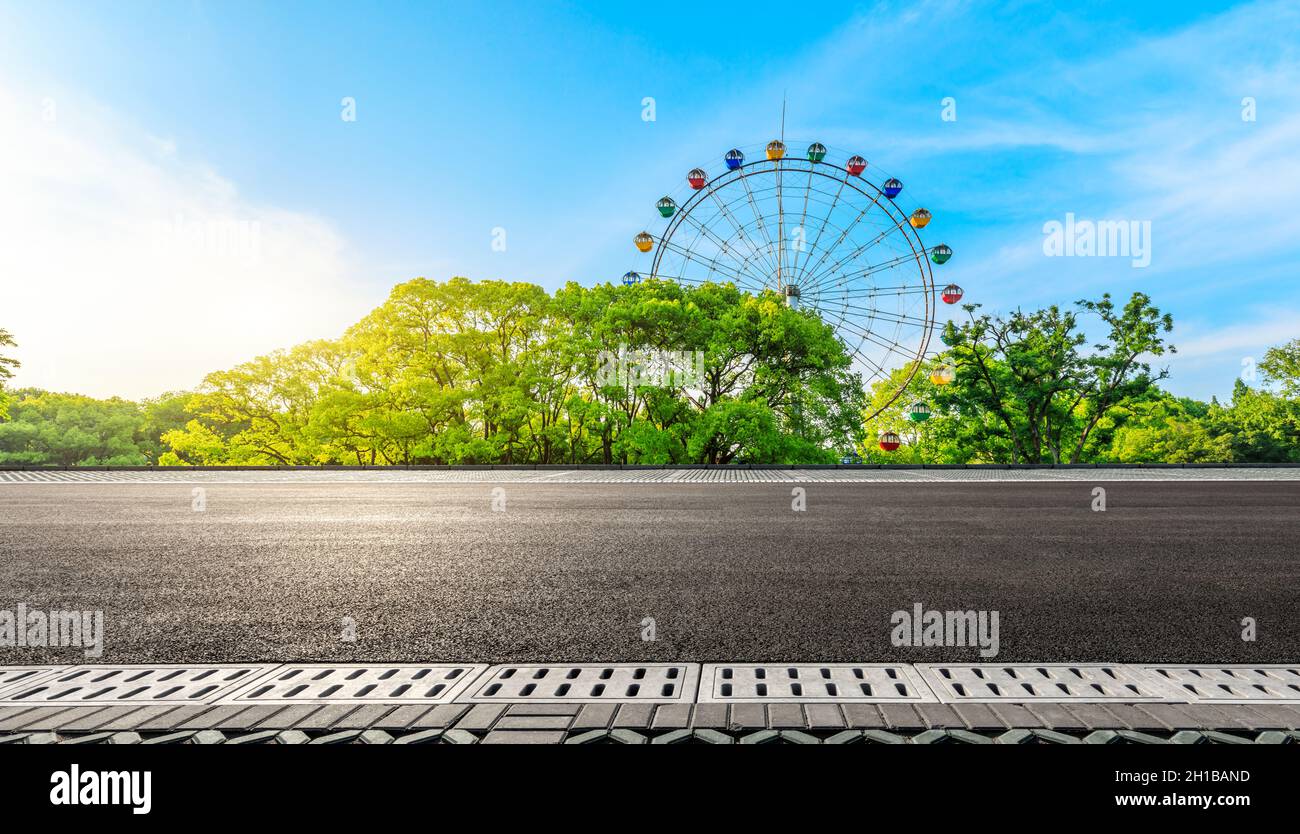 Strada asfaltata vuota e ruota di ferro con foresta verde sotto il cielo blu. Foto Stock