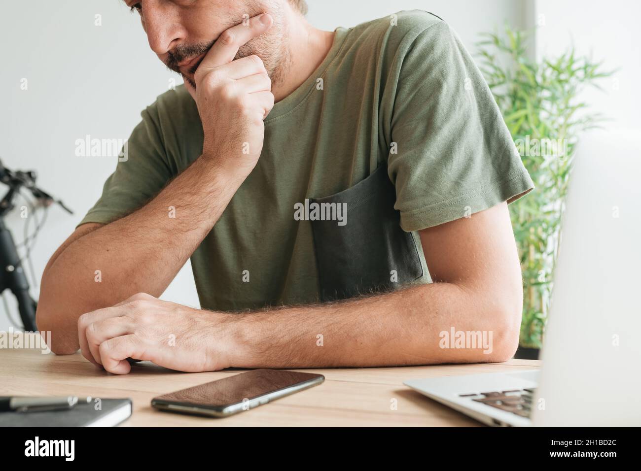 Telelavoro seduto alla scrivania di casa e pensare con mano sul mento per attività di lavoro remoto, fuoco selettivo Foto Stock