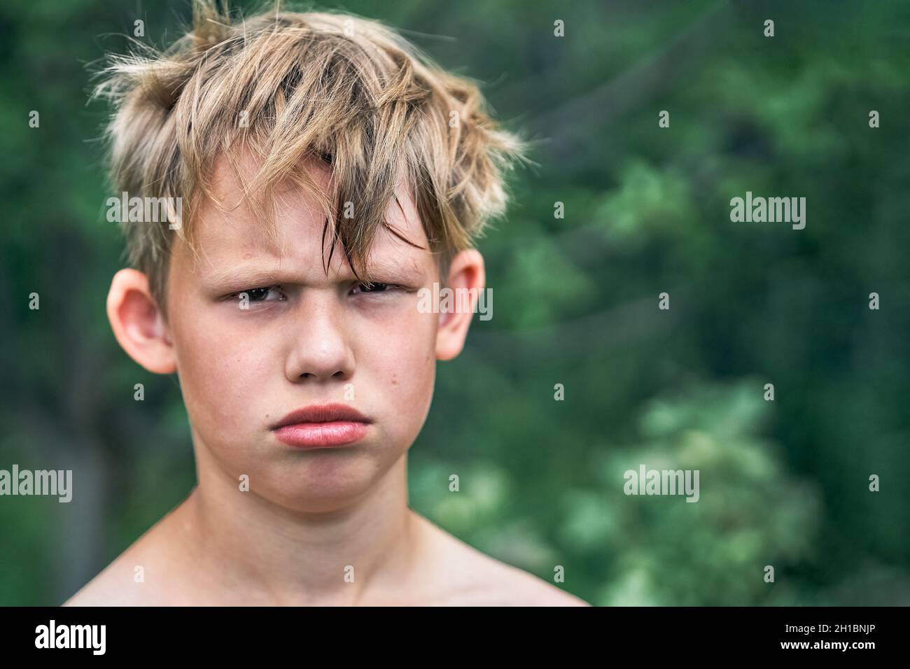 Offeso ragazzo scuola junior con bionda capelli ruvidi in posa per la macchina fotografica nel parco verde in bella estate giorno vista da vicino Foto Stock