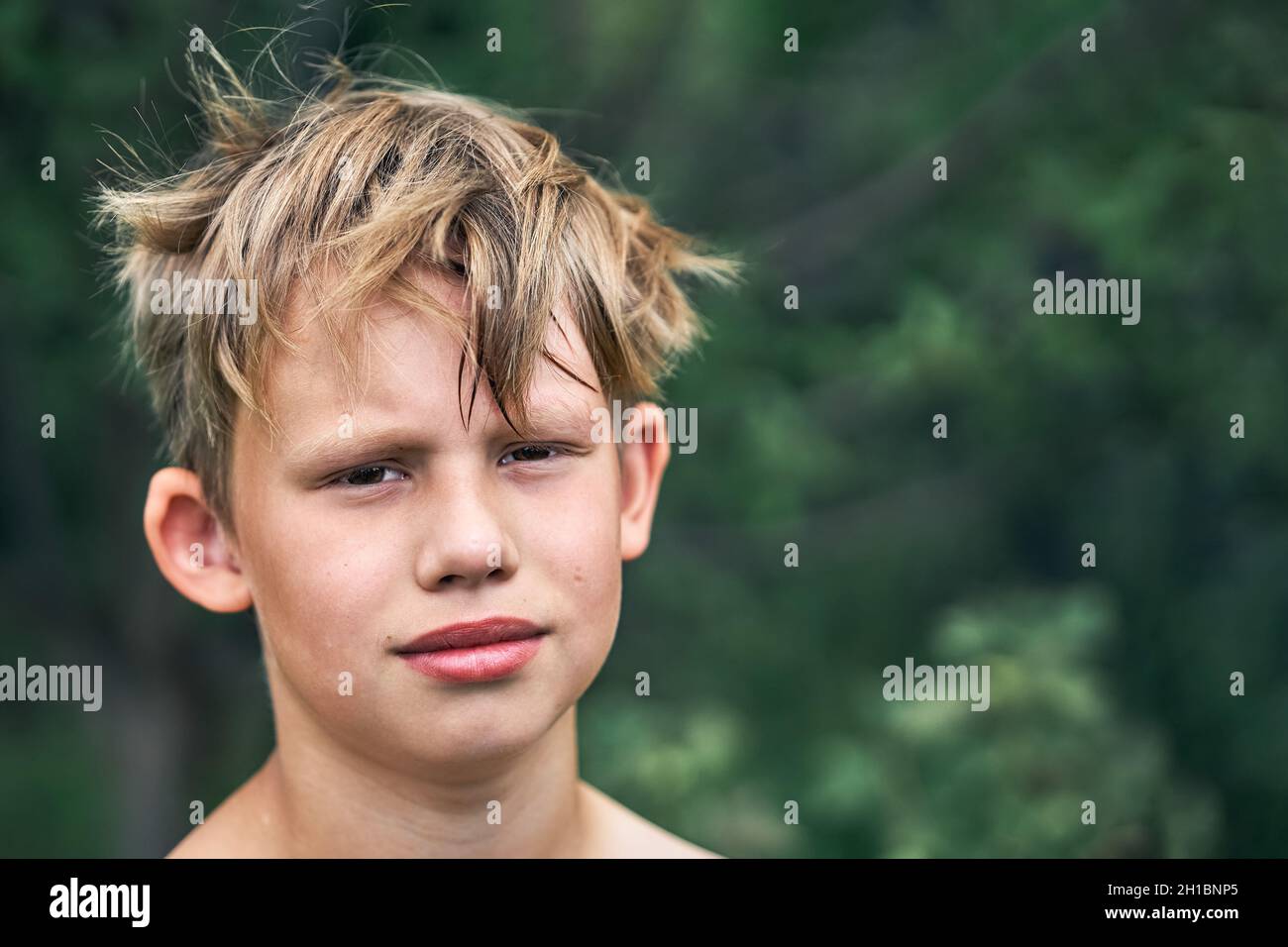 Scolaro giovane che sorride finto con capelli biondi grovigli ruvidi in posa per la macchina fotografica nel parco verde in bella vista giorno d'estate vicino Foto Stock