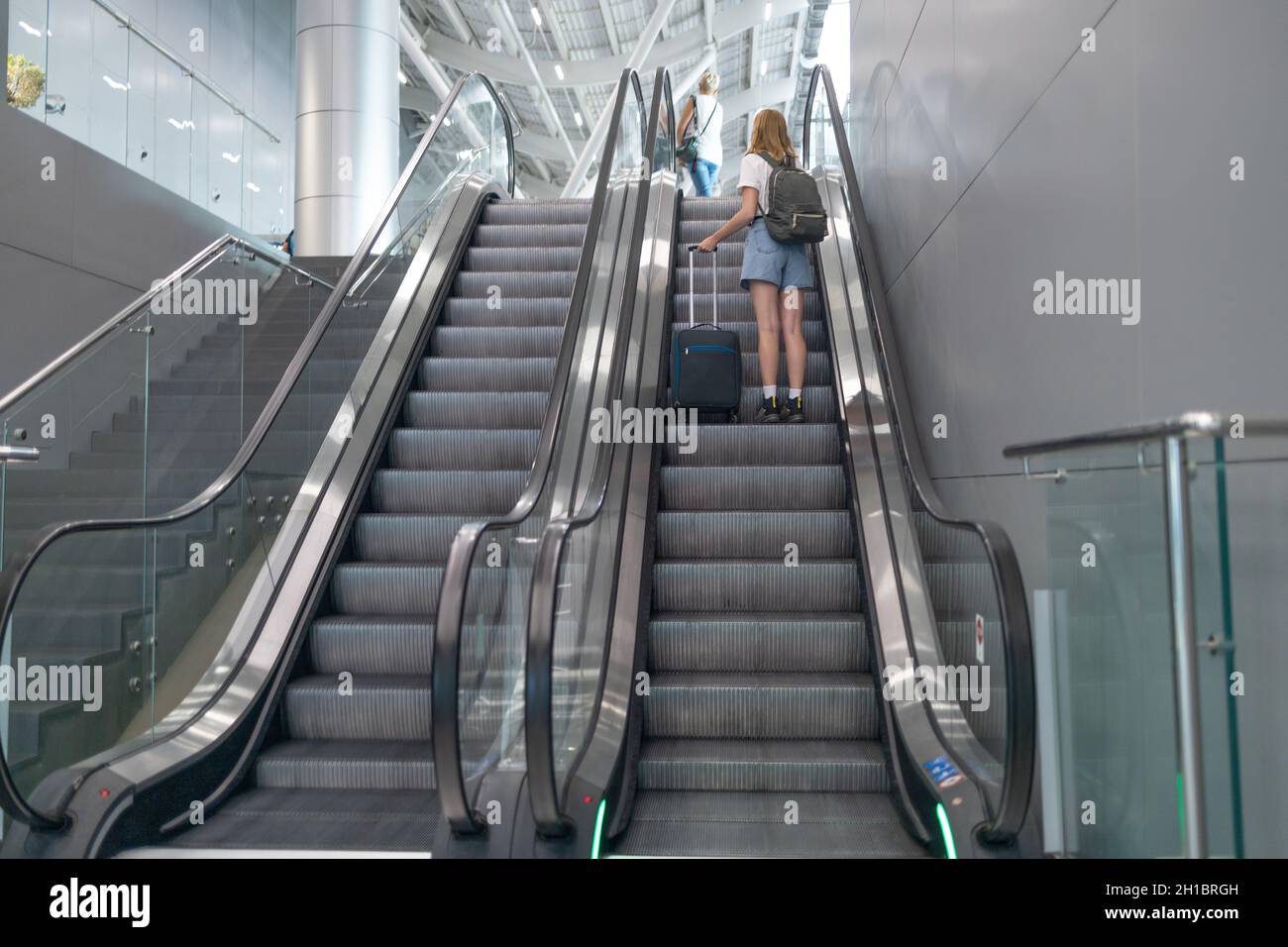 Turista nel terminal dell'aeroporto in piedi presso la scala mobile. Passeggero donna che viaggia in aereo durante la pandemia del virus covid19 Foto Stock