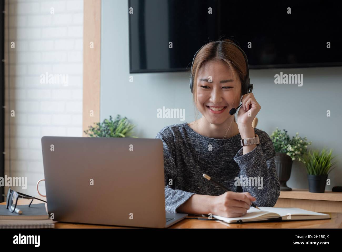 Primo piano giovane donna asiatica imparare classe online utilizzando un computer portatile e scrivere notebook sul posto di lavoro, apprendimento e e concetto di lavoro online. Foto Stock