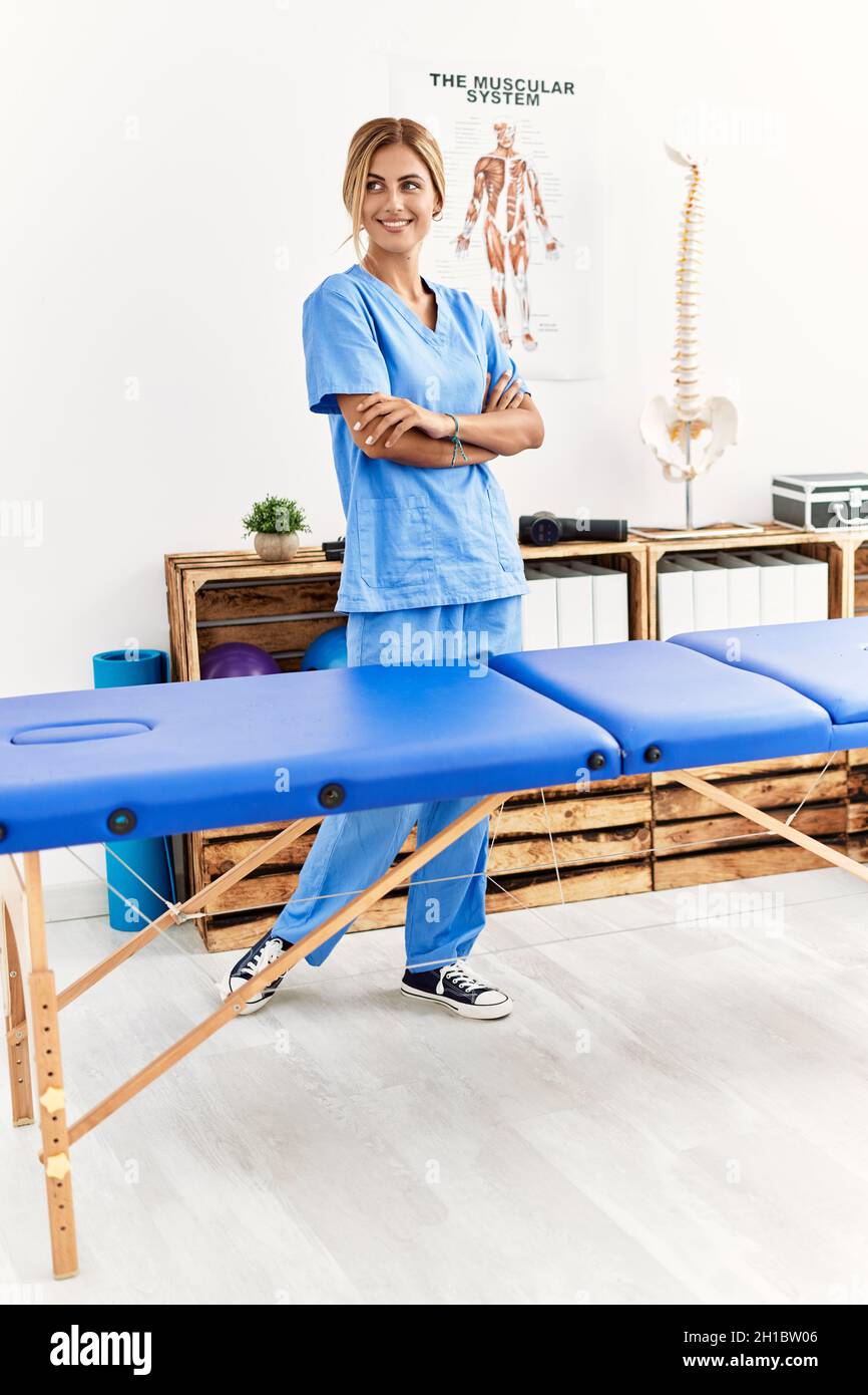 Giovane fisioterapista caucasico sorridente felice in piedi con le braccia incrociate gesto alla clinica Foto Stock