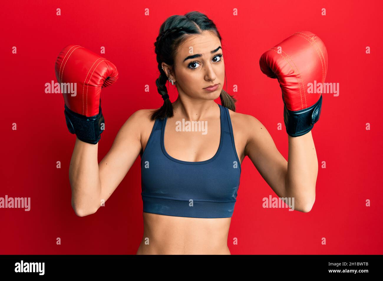 Giovane ragazza bruna usando i guanti di boxing che indossano le trecce  senza indizio e confuso espressione. Concetto di dubbio Foto stock - Alamy