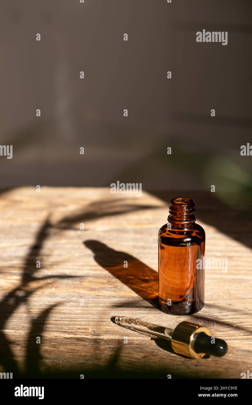Bottiglia di vetro ambrato scuro con contagocce per olio, lozione o siero su sfondo di legno invecchiato con un'ombra dura di foglie di palma tropicali. Presentazione di un prodotto cosmetico. Disposizione del salone di bellezza . Foto Stock