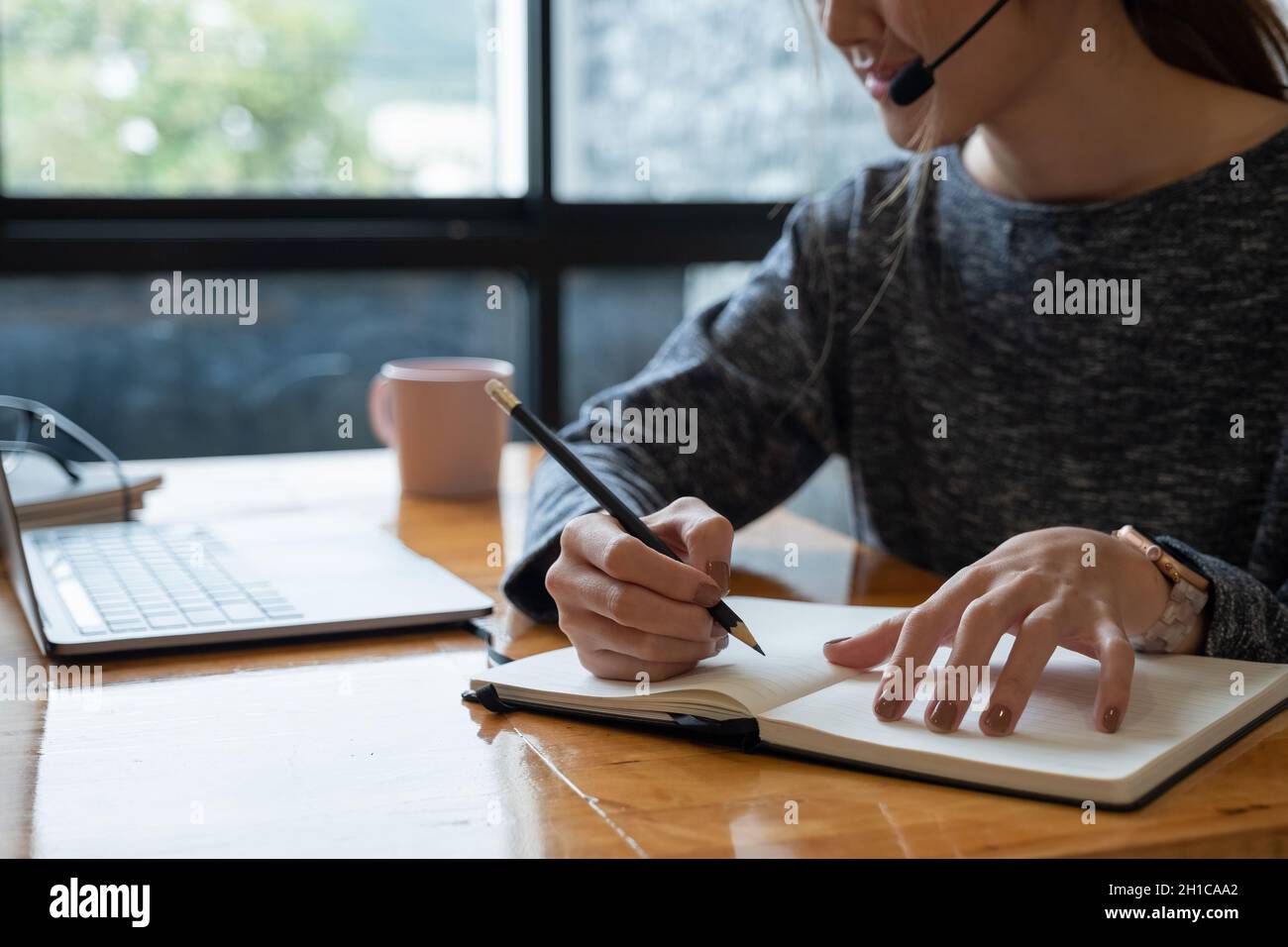 Primo piano mano di donna asiatica che studia online da casa facendo appunti per gli studenti imparare a distanza su laptop facendo i compiti, guardando il video di ascolto Foto Stock