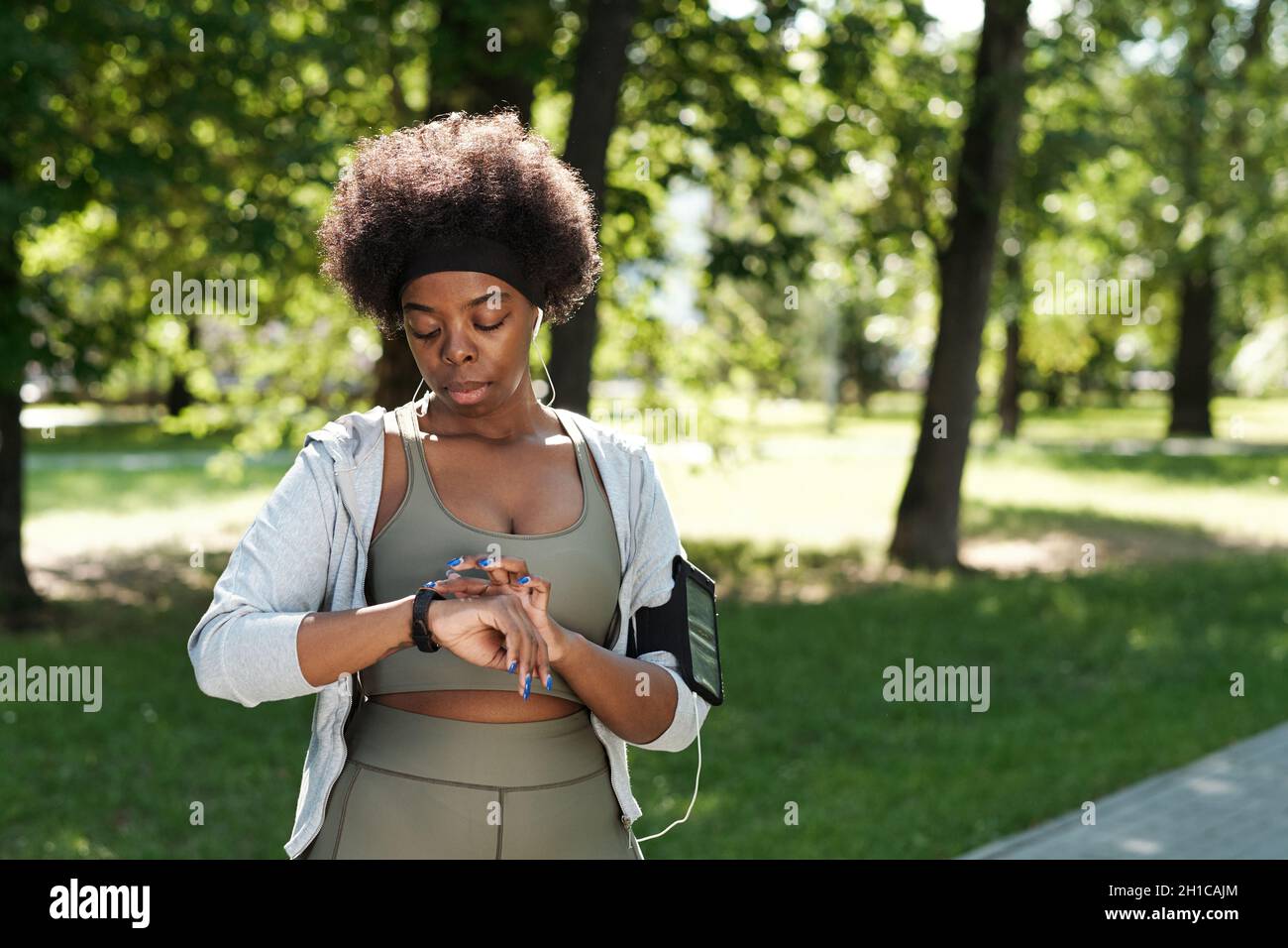 Giovane donna africana in abbigliamento sportivo che guarda lo smartwatch durante l'allenamento nel parco Foto Stock