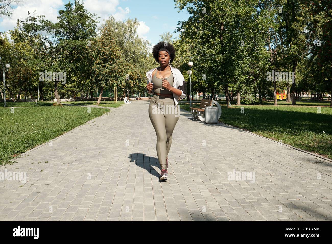 Giovane attiva più grande femmina jogging lungo la strada tra prati verdi nel parco Foto Stock