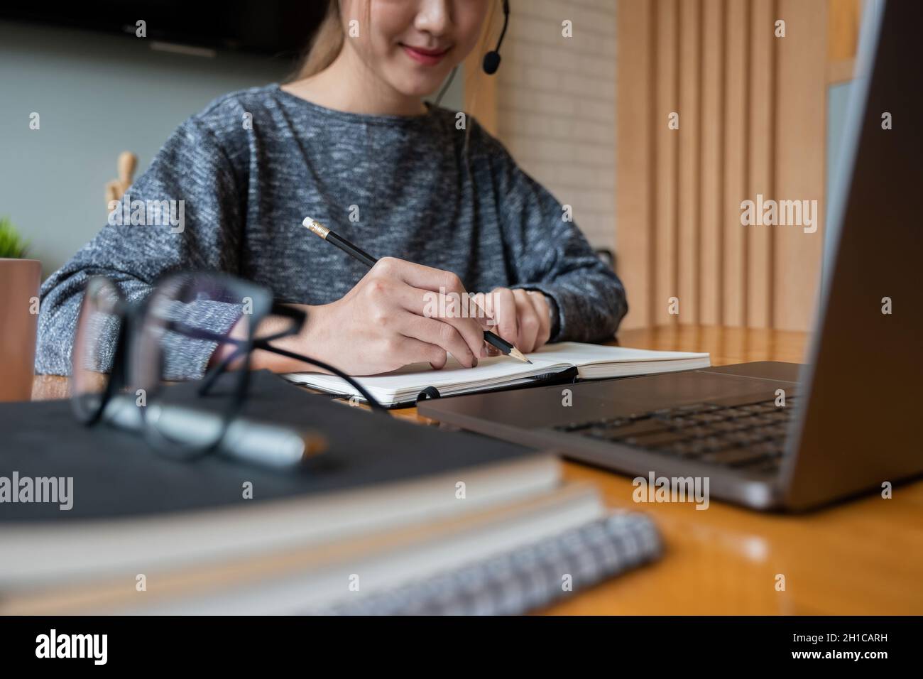 Primo piano mano di donna asiatica che studia online da casa facendo appunti per gli studenti imparare a distanza su laptop facendo i compiti, guardando il video di ascolto Foto Stock