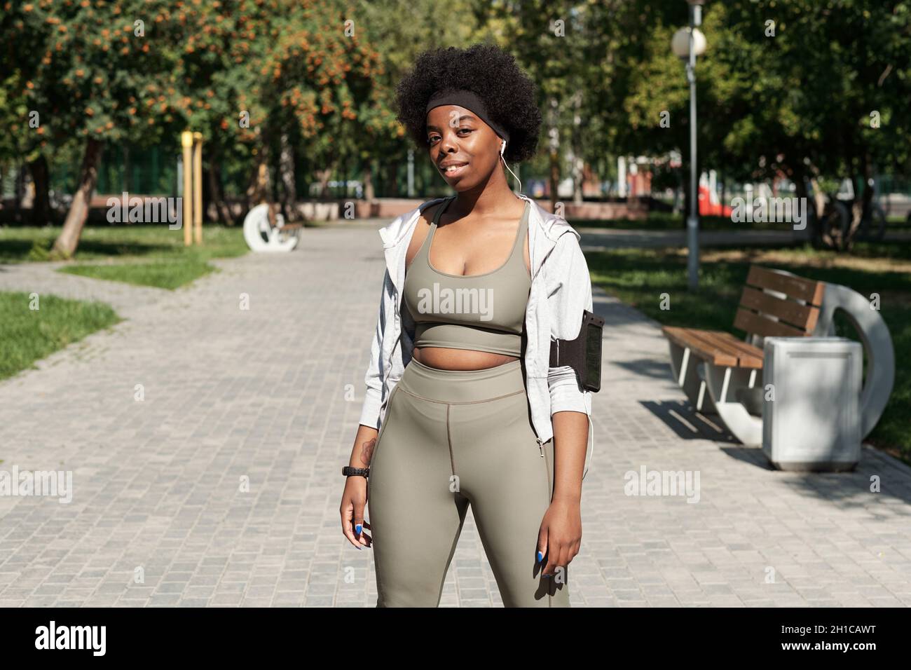 Donna felice attiva in abbigliamento sportivo che ti guarda mentre sei in piedi su strada nel parco Foto Stock