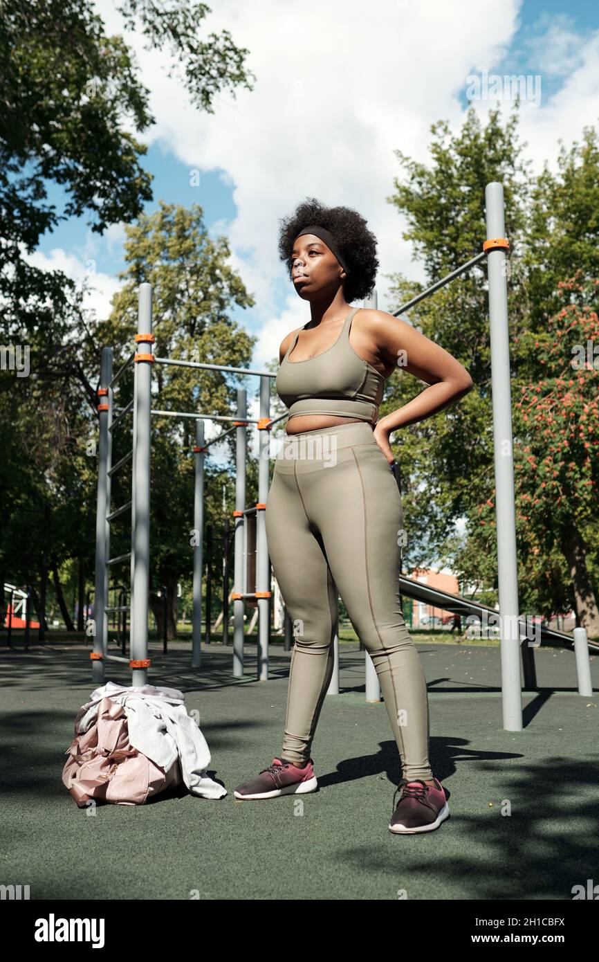 Giovane donna di taglia Plus in abbigliamento sportivo grigio in piedi sul terreno sportivo nel parco al mattino Foto Stock
