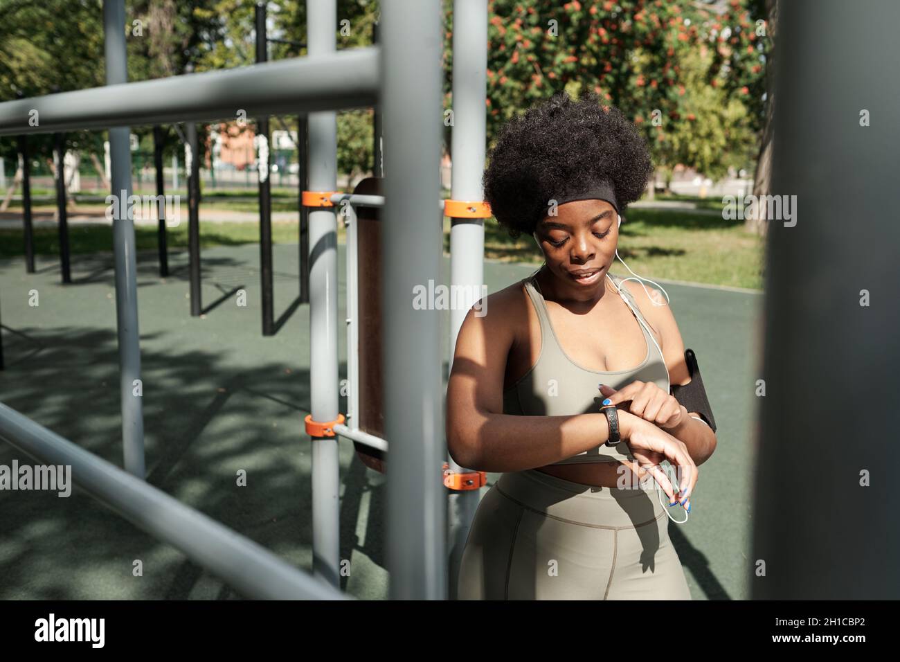 Giovane donna in abbigliamento sportivo che guarda lo smartwatch al polso dopo l'allenamento sul terreno sportivo Foto Stock