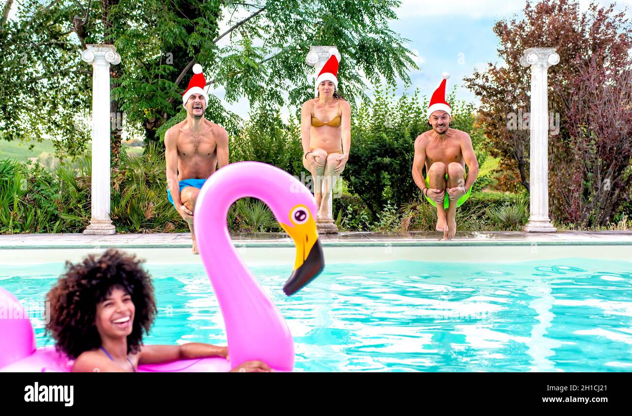 buon natale! felice gruppo vario di amici che indossano natale santa hat divertirsi a piscina partito saltare in acqua insieme celebrare Foto Stock