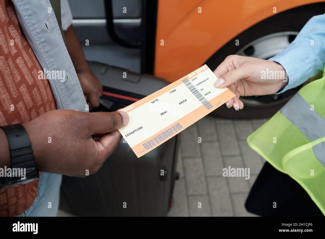 Mano di passeggero africano con valigia che passa il suo biglietto a giovane conduttore femminile Foto Stock