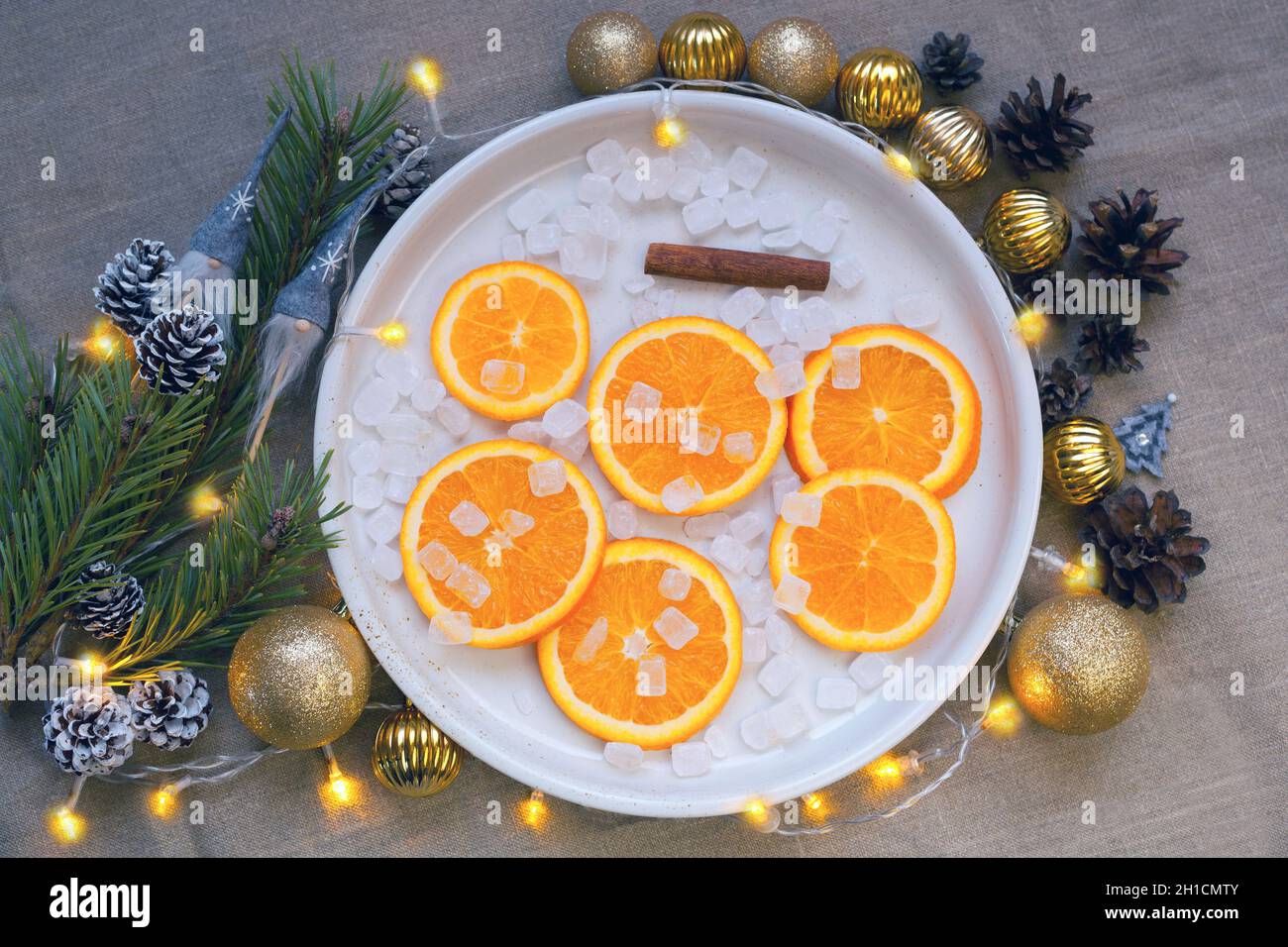 arance al piatto vicino albero di natale ramo, palle d'oro e coni di pino. Decorazioni tangerine Foto Stock