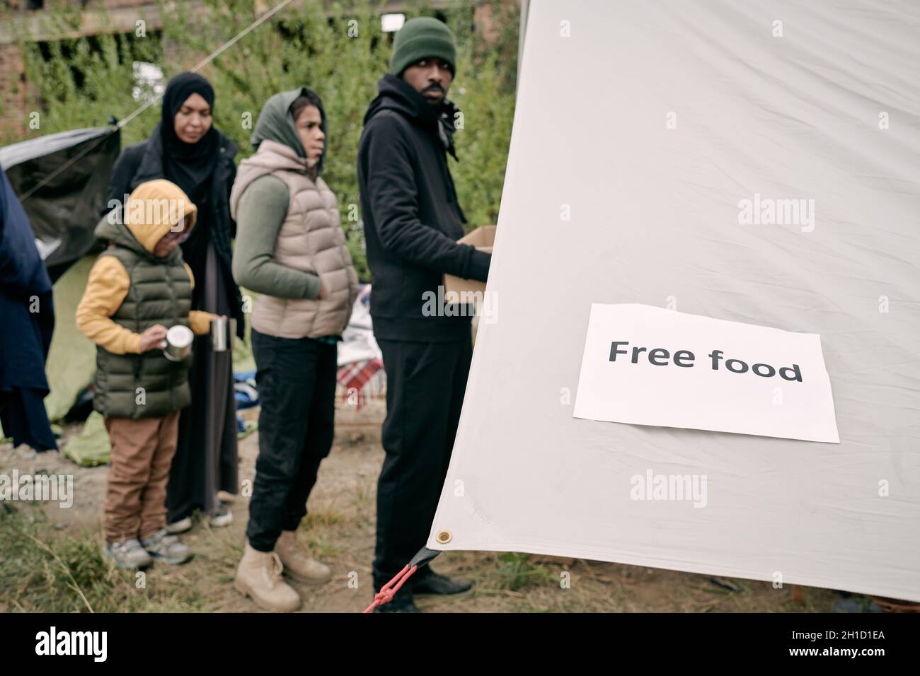 Fila di migranti che si trovano di fronte alla tenda del volontariato per ottenere del cibo gratuito Foto Stock