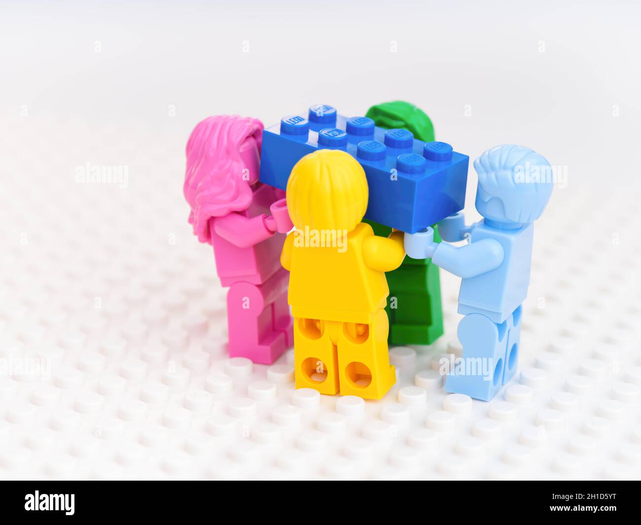 Tambov, Federazione russa - 17 ottobre 2021 quattro minifigure Lego monocromatiche che trasportano un mattone Lego blu. Sfondo bianco. Foto studio. Foto Stock