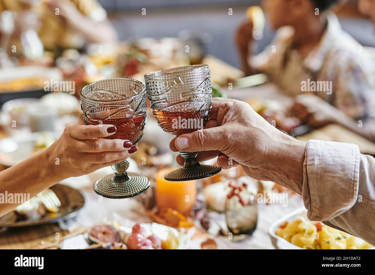 Primo piano di una coppia anziana che tostava con bicchieri di vino rosso mentre si siede al tavolo da pranzo con la famiglia Foto Stock