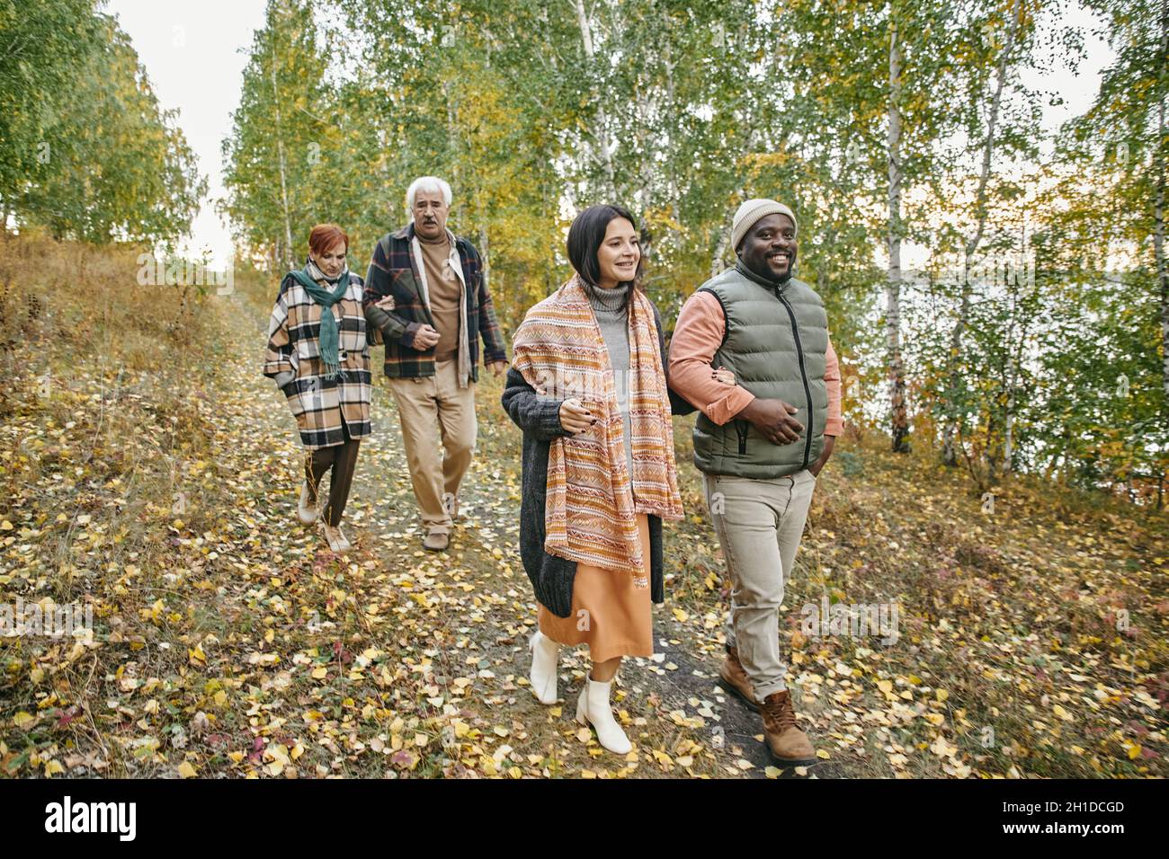 Due generazioni di famiglia che camminano insieme nella foresta autunnale, parlano e si godono la natura Foto Stock
