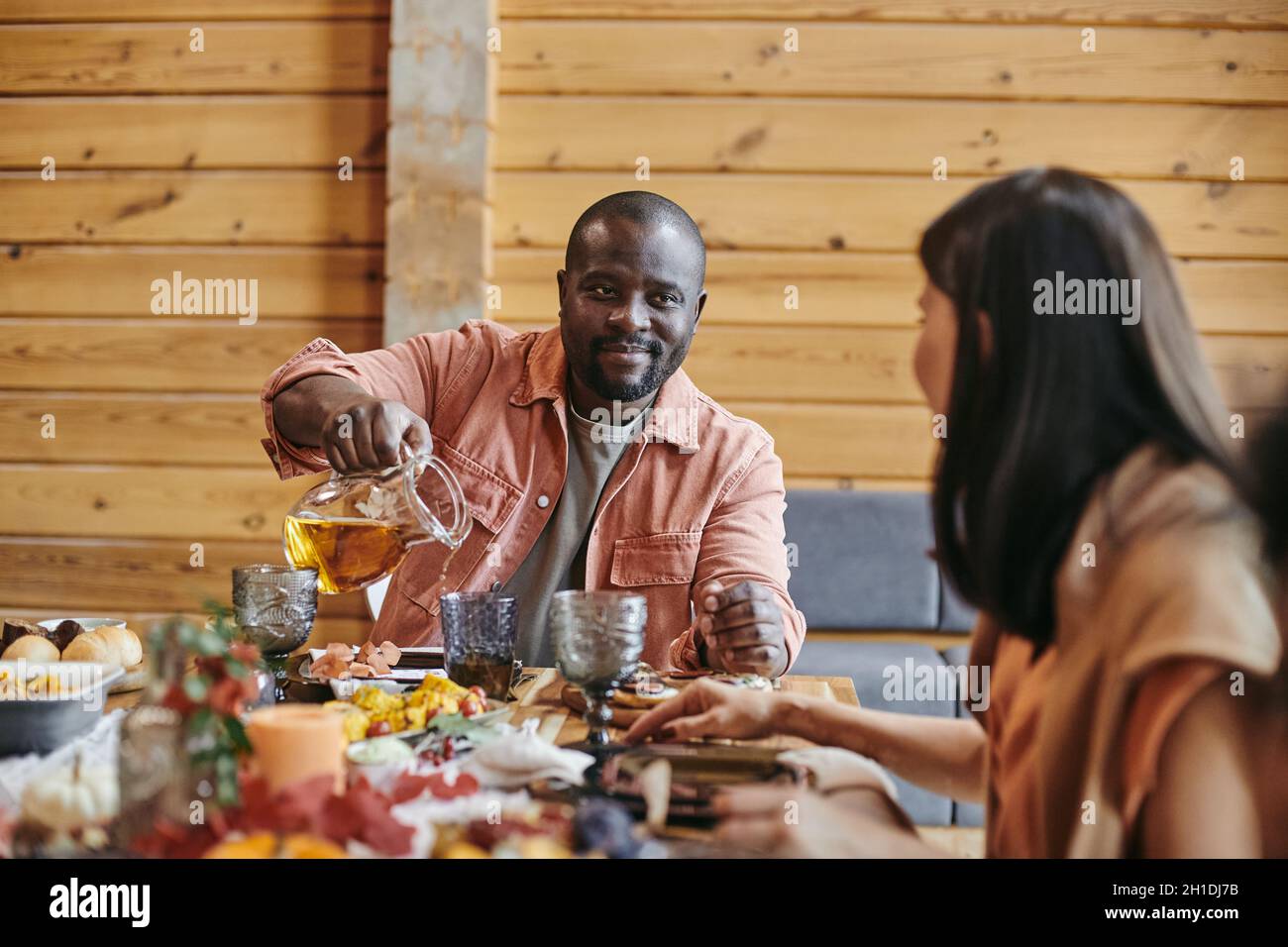 Il giovane africano che versa il succo nel bicchiere e parla con la donna al tavolo da pranzo Foto Stock