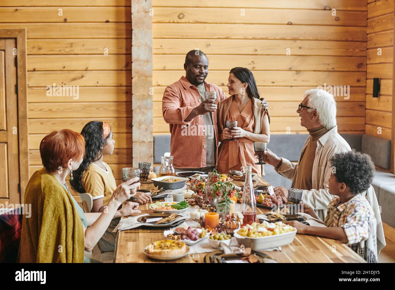 Giovani coppie che si congratulano con i loro genitori, si levano in piedi e dicono il toast durante la cena al tavolo delle feste Foto Stock