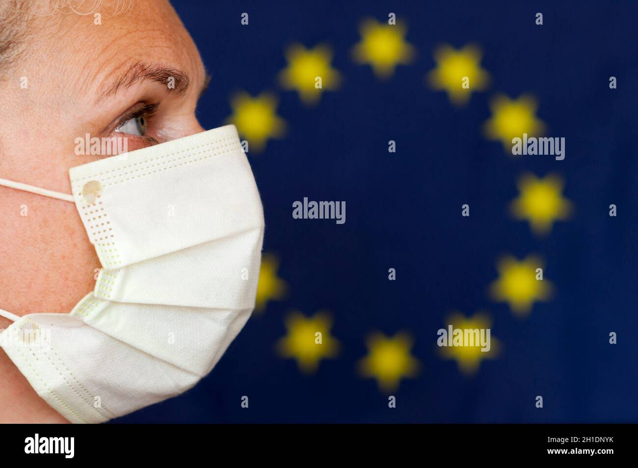 Donna con maschera di fronte alla bandiera dell'Unione europea in profilo. Foto Stock
