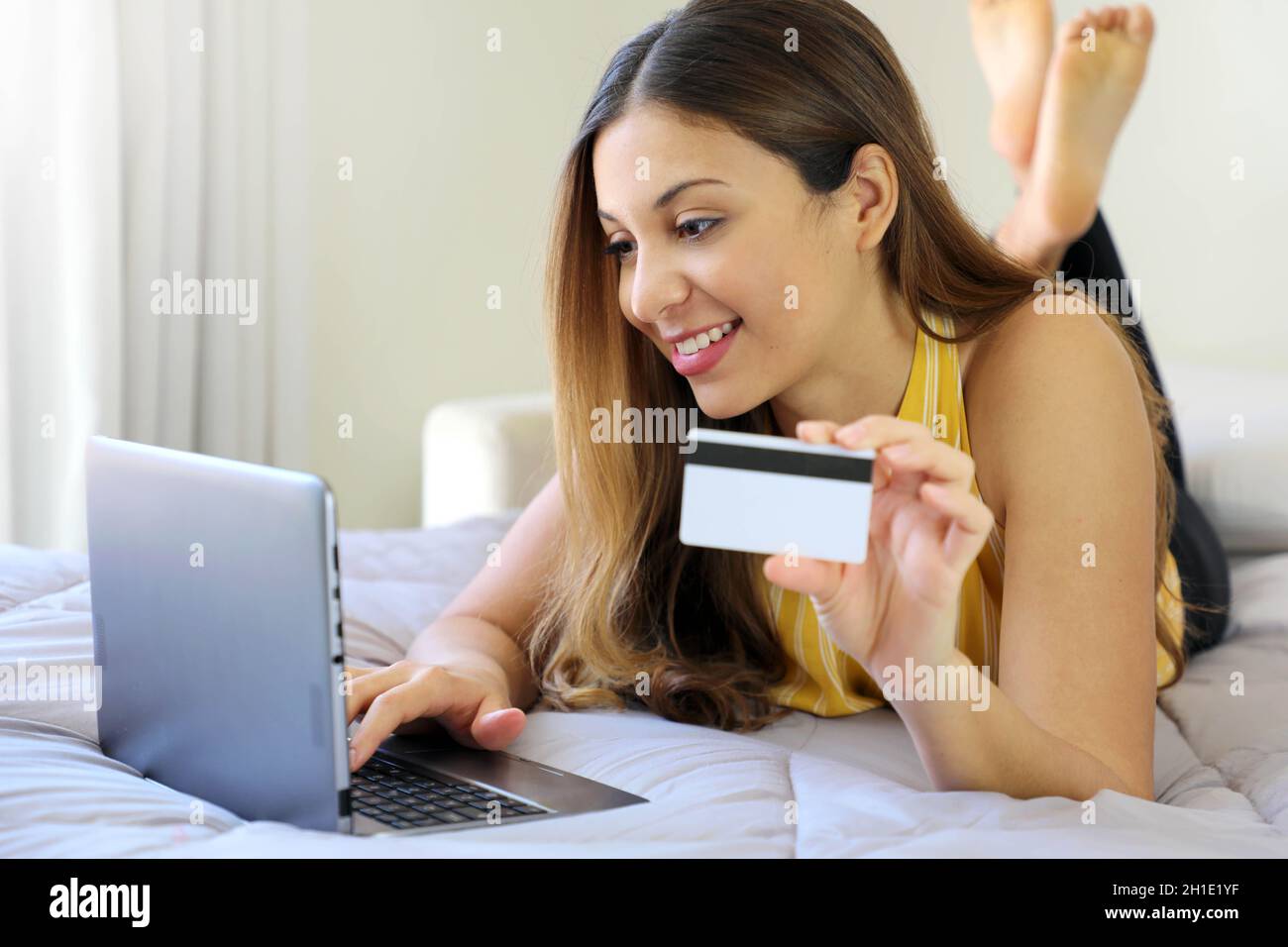 Sorridente giovane donna rilassata sdraiata sul letto inserire il numero di carta di credito sul notebook facendo shopping sicuro online a casa Foto Stock
