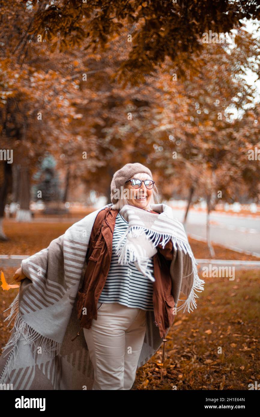 Stagione autunnale. Donna adulta felice anni '50 in un berretto di lana e  abiti boho accogliente a piedi nel parco della città autunno. Lady in  occhiali accessori minimal Foto stock - Alamy