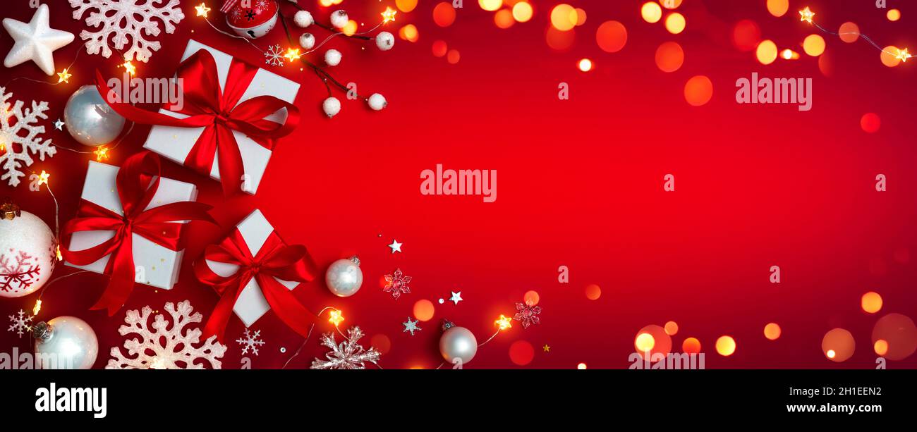 Confezioni regalo su rosso con ornamenti natalizi - regali con luci bokeh e fiocchi di neve Foto Stock