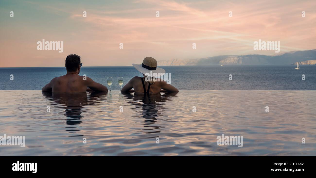 la coppia gode di una vista romantica sul mare e beve champagne nella piscina a sfioro del resort di lusso. spazio per la copia di striscioni Foto Stock