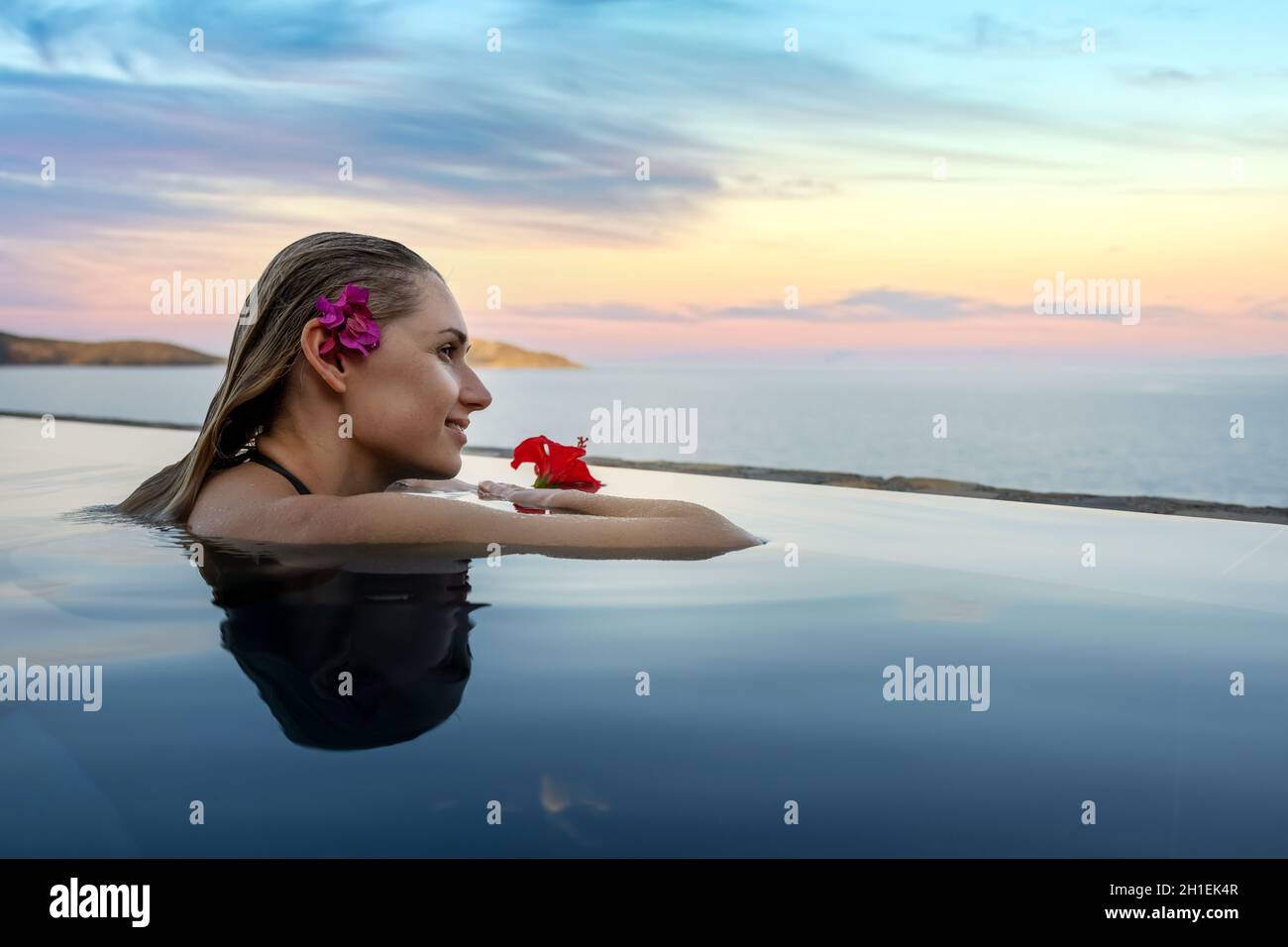 vacanza resort di lusso - donna con fiore nei capelli rilassante nella piscina a sfioro con vista mare. spazio copia Foto Stock