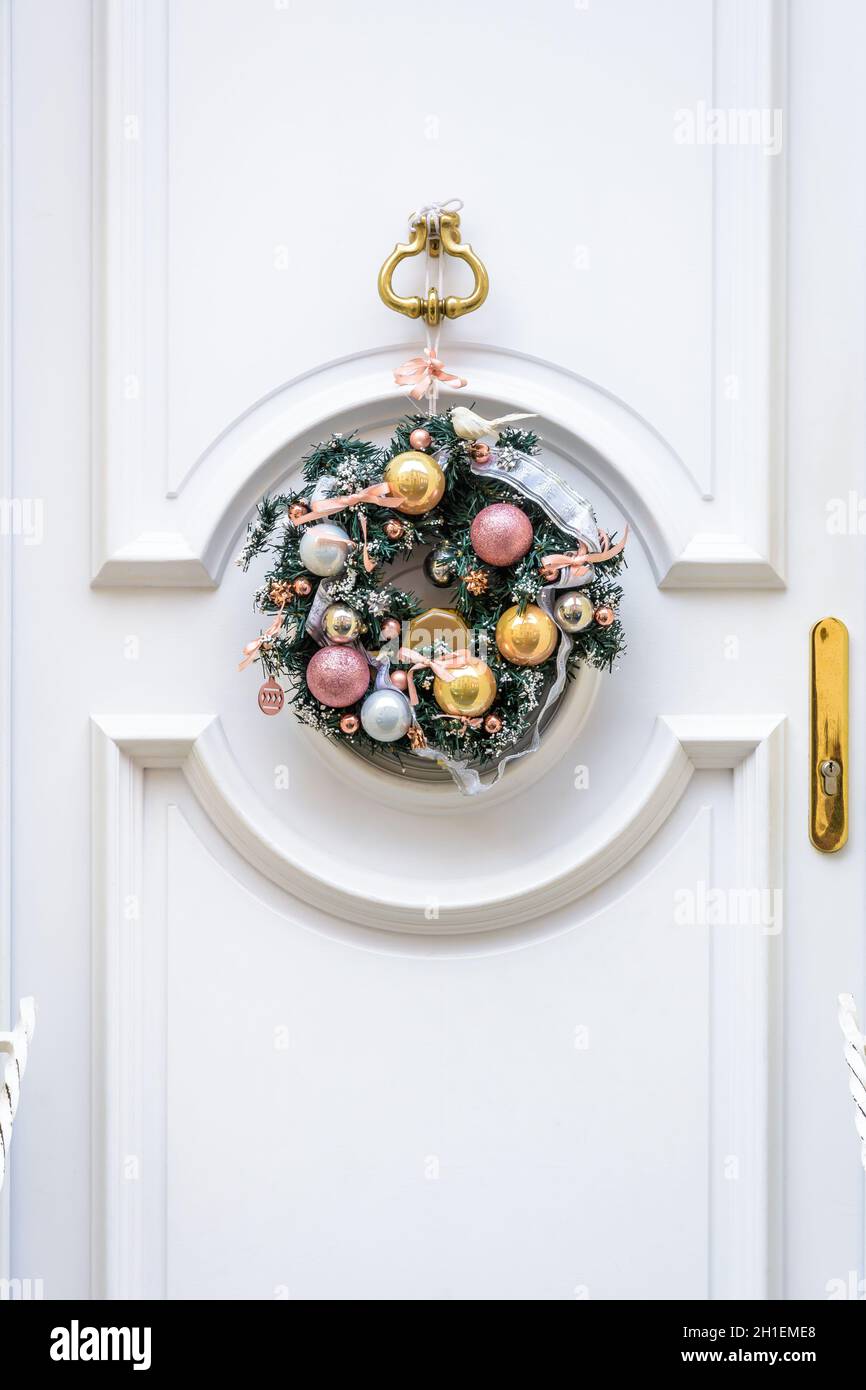 Vista frontale di una corona di Natale in rami di abete plastico con baubles e nastri, appesa su una porta frontale bianca con modanature. Foto Stock