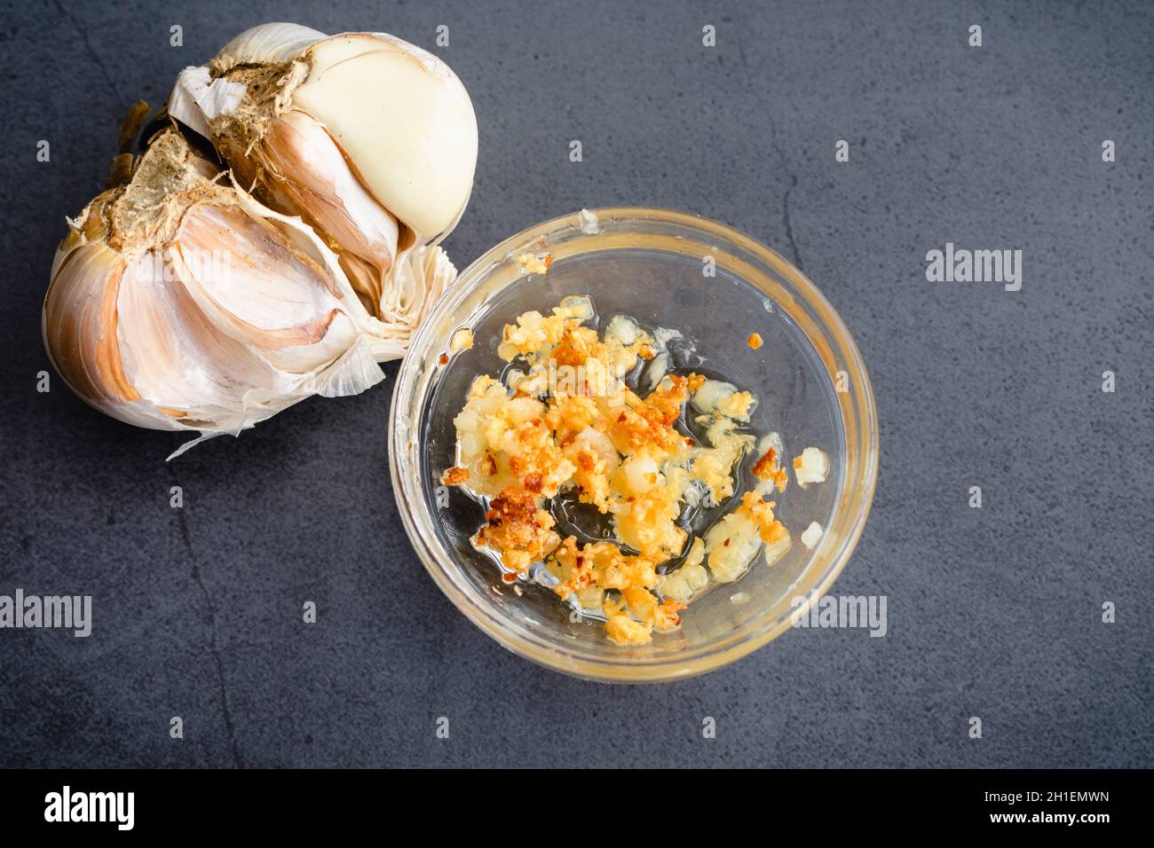 Aglio tritato rosolato in un piccolo recipiente per la preparazione: Fritti di aglio fresco con un bulbo d'aglio accanto Foto Stock