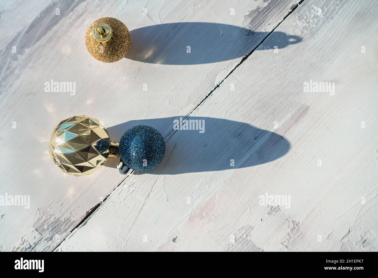 palle di natale blu brillante e dorato su sfondo bianco in legno alla luce del sole Foto Stock