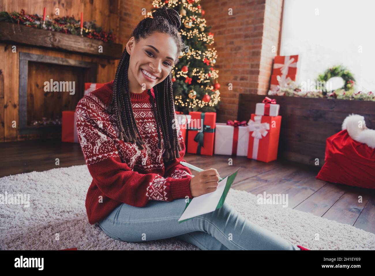 Ritratto di attraente ragazza allegra seduta su tappeto scrivere lettera wishlist newyear tradizione a casa decorata al chiuso Foto Stock
