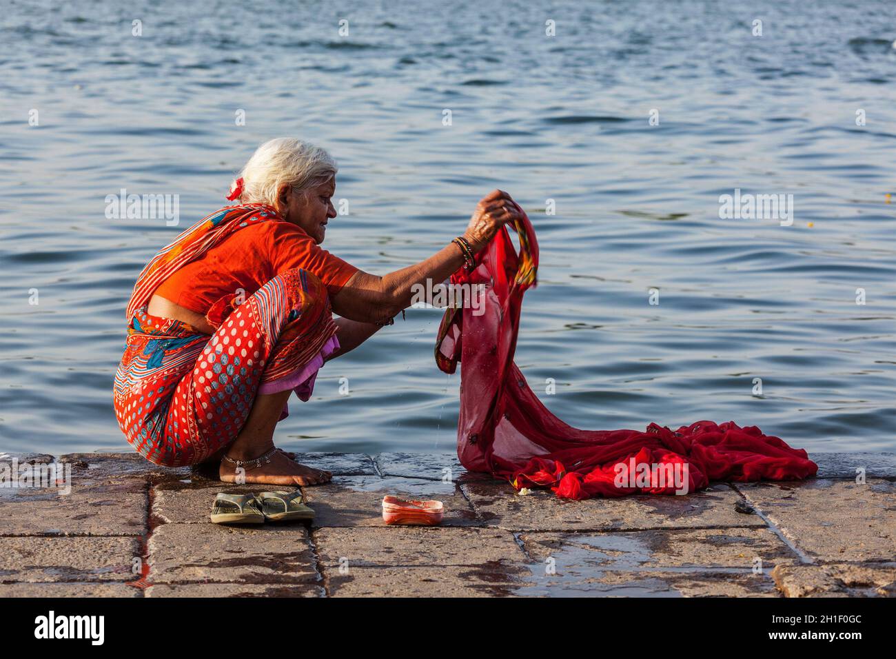 MAHESHWAR, INDIA - 26 APRILE 2011: Vecchia donna indiana lavaggio sari sul fiume sacro Narmada ghats. Agli Indù Narmada è uno dei 5 fiumi santi dell'India Foto Stock