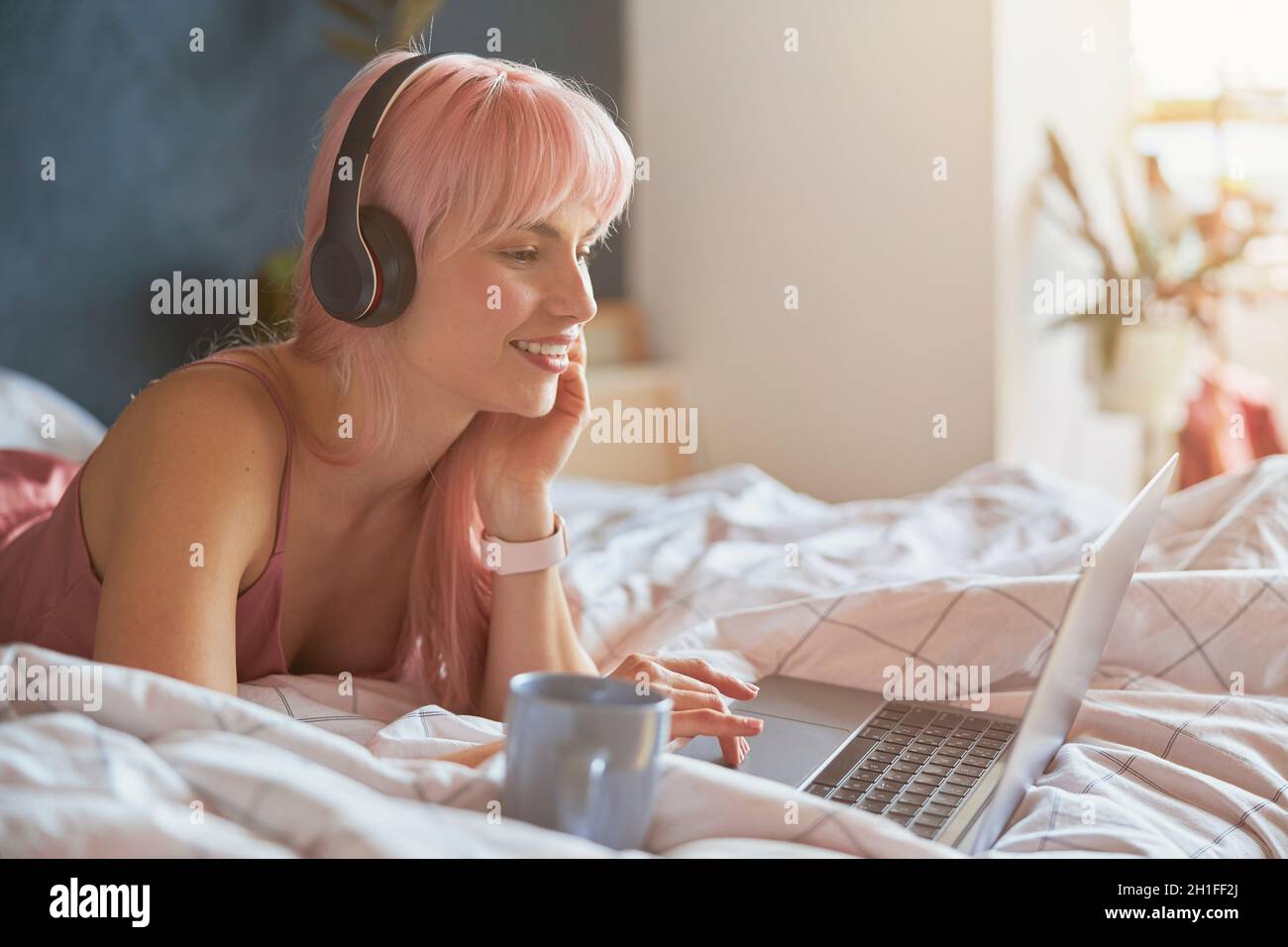 Signora felice con le cuffie e smartwatch surfs internet sdraiati su un comodo letto Foto Stock